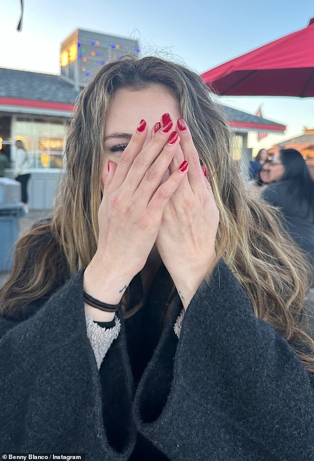 Снимки были сделаны на открытом воздухе: певица одета в черное шерстяное пальто и позирует с красными ухоженными руками возле лица.