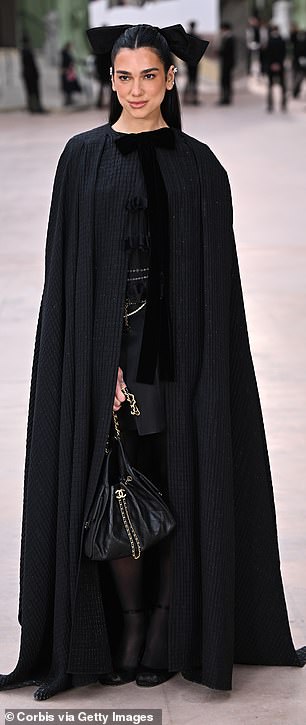 Dua Lipa Sled ее драматичный черный плащ с длинными полами на шоу Chanel на Paris Fashion Week во вторник